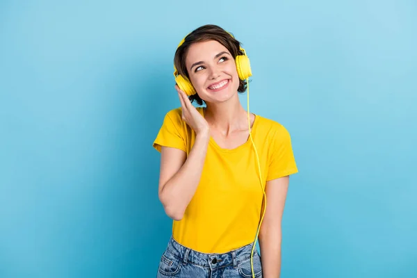 Foto de linda chica escuchar música buscar espacio vacío usar auriculares amarillo camiseta aislado color azul fondo — Foto de Stock