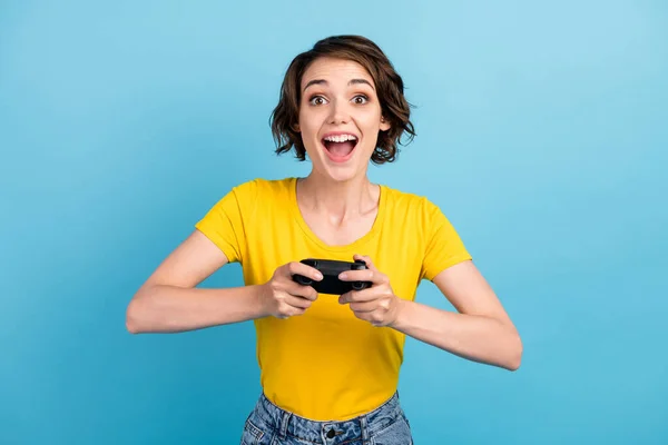 Foto van gek jong meisje houden gamepad open mond look camera dragen geel t-shirt geïsoleerde blauwe kleur achtergrond — Stockfoto