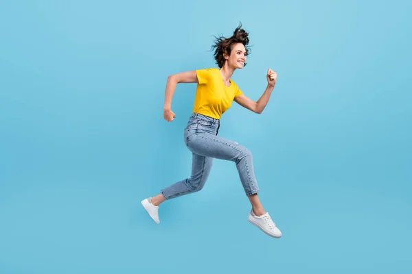 Full length profile photo of young lady jump run wear yellow t-shirt jeans sneakers isolated blue color background — Stock Photo, Image