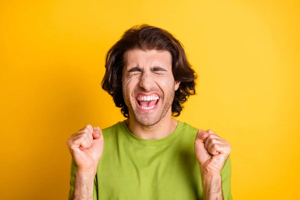 Foto di stupito divertente giovane uomo alzare i pugni chiuso gli occhi indossare verde t-shirt isolato colore giallo sfondo — Foto Stock