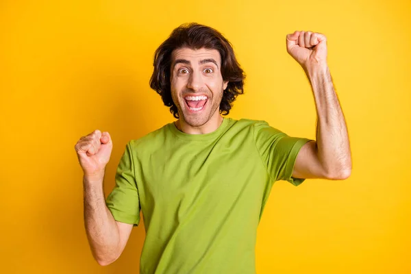 Fénykép izgatott funky fiatalember emelje öklével nyitott száj viselni zöld póló elszigetelt sárga színű háttér — Stock Fotó