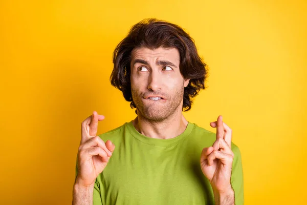 Foto de hombre joven nervioso morder los dedos cruzados buscar espacio vacío usar camiseta verde aislado color amarillo fondo — Foto de Stock