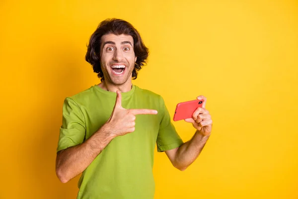 Foto van gekke opgewonden man hold telefoon geven vinger dragen groen t-shirt geïsoleerde gele kleur achtergrond — Stockfoto