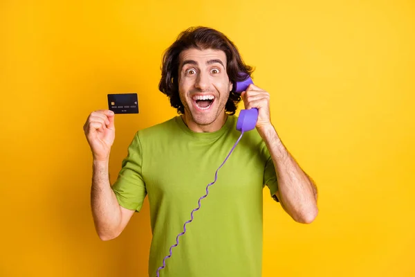 Foto de engraçado animado homem segurar telefone talk show cartão de débito desgaste verde t-shirt isolado cor amarela fundo — Fotografia de Stock