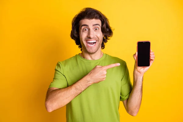 Foto de homem positivo segurar telefone tela de dedo direto espaço vazio desgaste verde t-shirt isolado cor amarela fundo — Fotografia de Stock