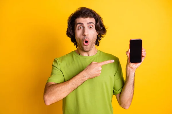 Foto de teléfono de retención chico indican la pantalla del dedo índice espacio vacío boca abierta desgaste camiseta verde aislado color amarillo fondo — Foto de Stock