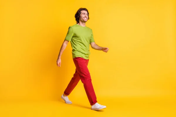 Tam boy vücut ölçülerinde, öne doğru aceleyle yürüyen kırmızı pantolonla gülümseyen bir adamın fotoğrafı. Canlı sarı arka planda izole edilmiş. — Stok fotoğraf