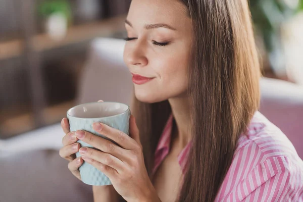 Foto de mulher de cabelos castanhos pacífica segurar caneca de café cheiro aroma olhos fechados dentro de casa dentro de casa em casa — Fotografia de Stock