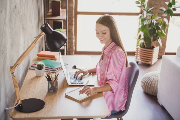 Perfil da foto lateral da morena jovem mulher sentar mesa escrever notebook laptop desgaste camisa listrada vermelha dentro de casa dentro de casa — Fotografia de Stock