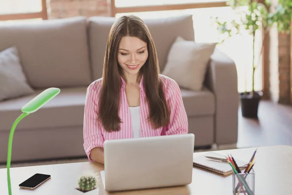 Foto de brillante adorable joven mujer vestida camisa a rayas sentada mesa escribiendo gadget moderno dentro de la habitación interior — Foto de Stock