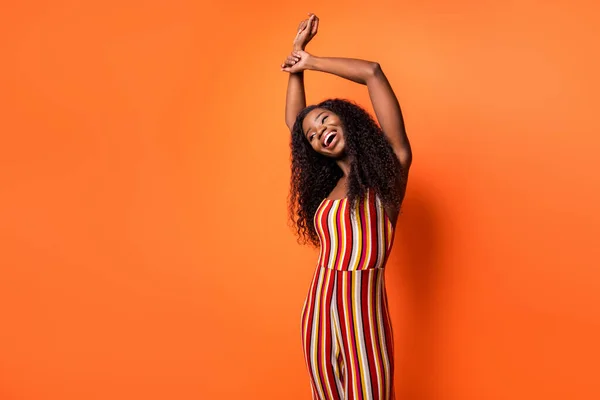 Foto van gelukkig mooi mooi Afrikaans amerikaans jong dame verhogen handen danser geïsoleerd op oranje kleur achtergrond — Stockfoto