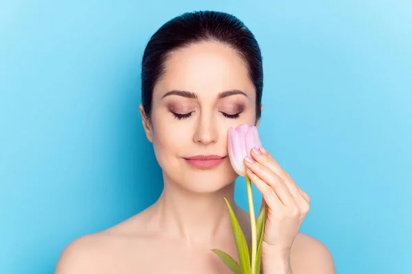Retrato de atraente na moda calma mulher nua pacífica tocando bochecha tulipa cosmética isolada sobre fundo de cor azul brilhante — Fotografia de Stock