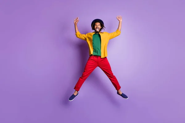 Foto de cuerpo entero de chico alegre de piel oscura vestido camisa amarilla saltando brazos de gran altura manos aisladas color púrpura fondo — Foto de Stock
