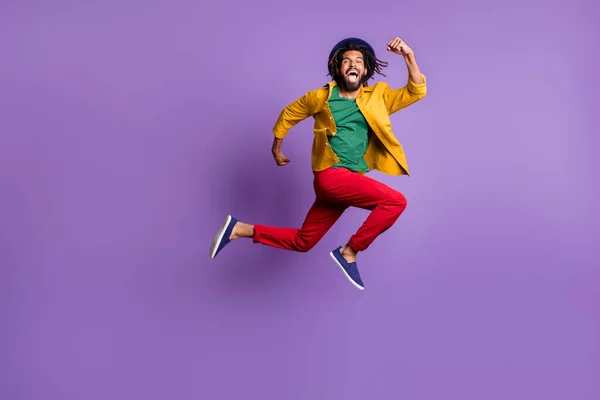 Foto de comprimento total de engraçado homem de pele escura usar gorro camisa amarela saltando alto apressando compras isolado cor violeta fundo — Fotografia de Stock