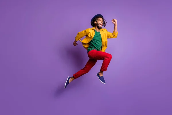 Volledige lengte foto van funky donkere huid guy gekleed geel shirt hoofddeksel springen snel geïsoleerde paarse kleur achtergrond — Stockfoto