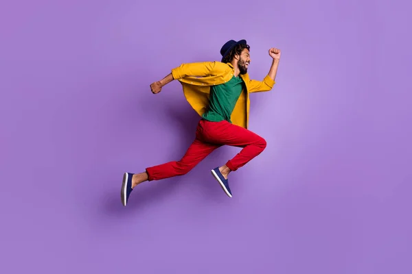 Lunghezza completa foto di intenzionale ragazzo pelle scura vestito camicia gialla copricapo salto corsa veloce isolato colore viola sfondo — Foto Stock