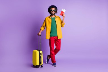 Full size photo of handsome dark skin guy beaming smile hold passport suitcase isolated on violet color background clipart