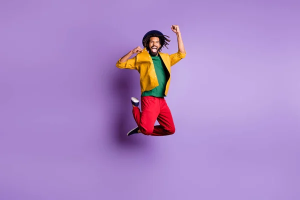 Foto de cuerpo entero de hombre de piel oscura con suerte usar camisa amarilla saltando puños altos aislados color violeta fondo —  Fotos de Stock