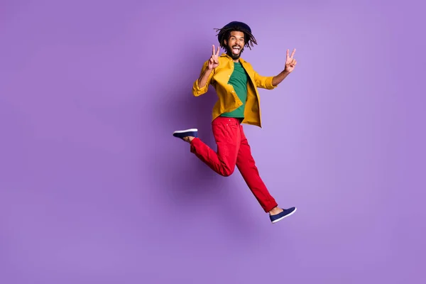 Foto de cuerpo entero de chico alegre de piel oscura vestido camisa amarilla mostrando v-signo de dos brazos aislados color púrpura fondo —  Fotos de Stock