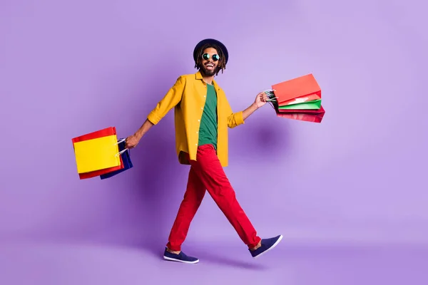 Foto de comprimento total de doce bonito pele escura cara vestido camisa amarela andando segurando sacos de compras isolado cor roxa fundo — Fotografia de Stock