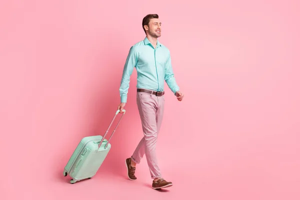 Pełna długość ciała rozmiar zdjęcie szczęśliwego człowieka z walizką będzie do terminalu na lotnisku uśmiechnięty izolowany na pastelowym tle różowy kolor — Zdjęcie stockowe
