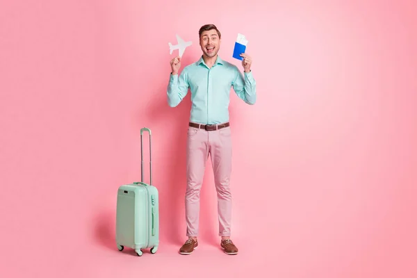 Full length body size photo of happy man with baggage keeping plane figure showing documents ticket isolated on pastel pink color background — Stock Photo, Image