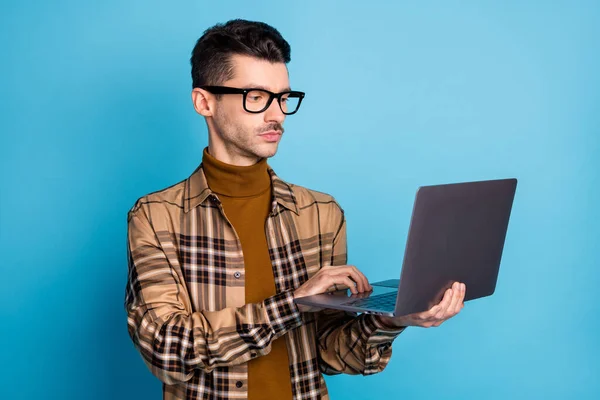 Foto av unga allvarliga fokuserad stilig man programmerare i glasögon som arbetar i bärbar dator isolerad på blå färg bakgrund — Stockfoto
