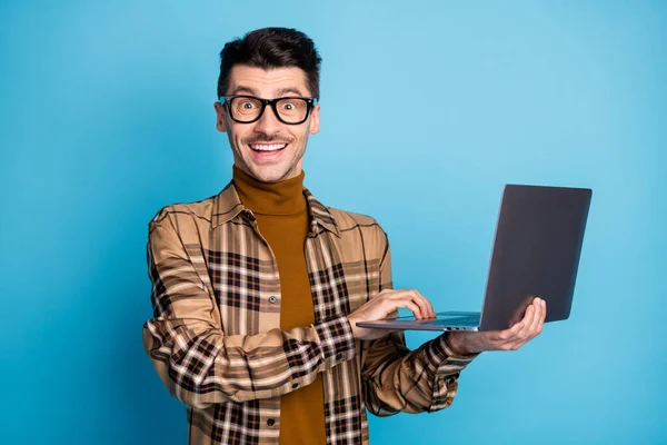 Foto de jovem bonito atraente animado alegre sorrindo positivo homem trabalhando em laptop isolado no fundo de cor azul — Fotografia de Stock