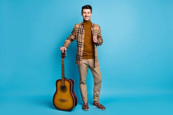 Полноразмерное фото улыбающегося позитивного молодого человека с акустической гитарой на голубом цветовом фоне — стоковое фото