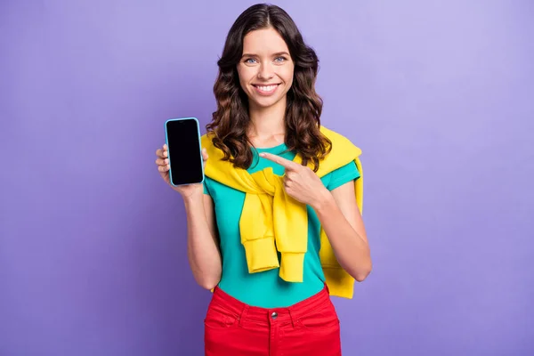 Retrato de menina de cabelos ondulados muito alegre segurando na mão demonstrando dispositivo recomendo isolado sobre fundo cor pastel violeta — Fotografia de Stock