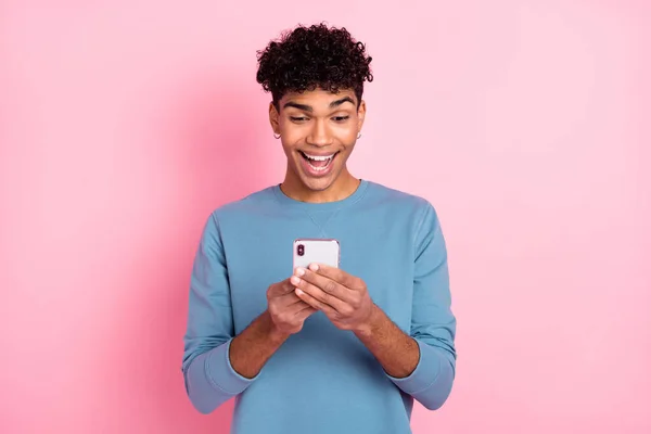 Foto retrato de un joven con piercing sorprendido leyendo noticias en el teléfono móvil aislado sobre fondo de color rosa pastel — Foto de Stock