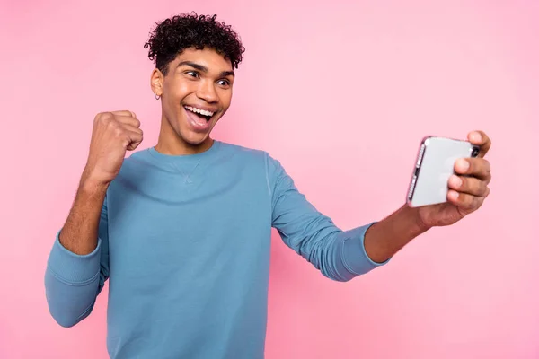 Retrato fotográfico del joven jugando juegos en el teléfono móvil haciendo gestos como ganador aislado sobre fondo de color rosa pastel — Foto de Stock
