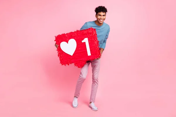 Foto de un joven negro feliz sonrisa positiva sostiene el corazón de papel piñata como icono social popular aislado sobre fondo de color rosa —  Fotos de Stock