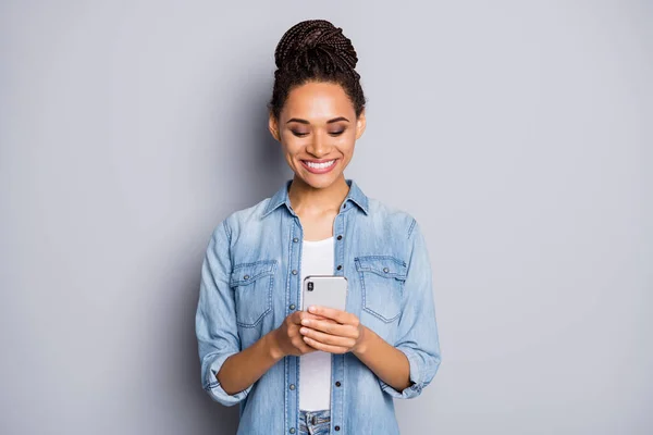 Foto portrét africké americké ženy s úsměvem psaní drží telefon ve dvou rukou izolovaných na jasné šedé pozadí — Stock fotografie