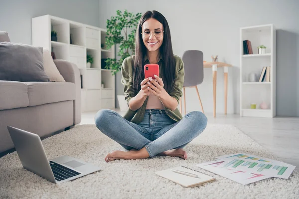 Full size portrait of attractive positive lady sit on floor look phone chatting have good mood working from home indoors — Stock fotografie