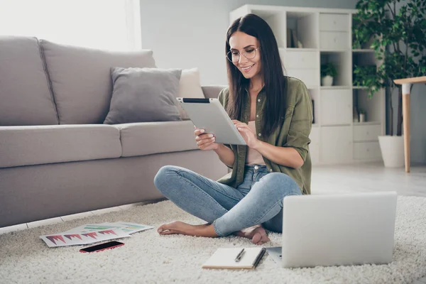 Portrait of pretty focused smart cheerful girl sitting on carpet using device analyzing finance market start-up at home house flat indoor — Stock fotografie