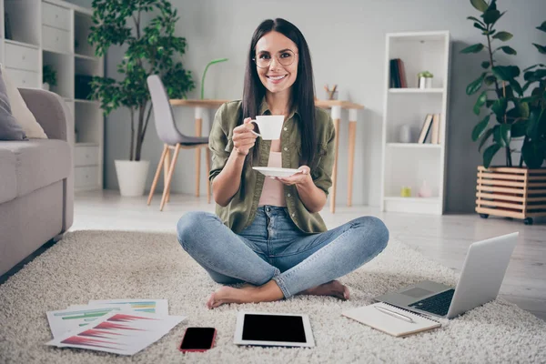 Full size portret van aantrekkelijke vrolijke persoon hand houden koffie zitten op de vloer tanden glimlach kijken camera thuis — Stockfoto
