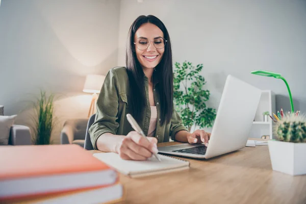 Portrait of charming cheerful girl sit behind desk arm hold pen take notes toothy smile enjoy working from home indoors — Stock fotografie