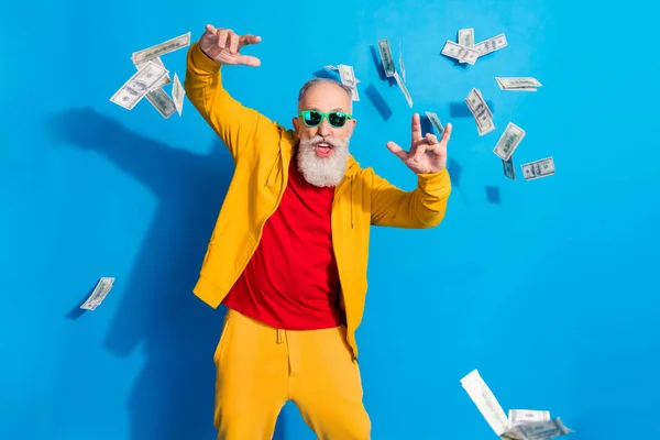 Fénykép funky boldog vidám mosolygós nagyapa napszemüvegben körülvéve repülő pénz elszigetelt kék színű háttér — Stock Fotó