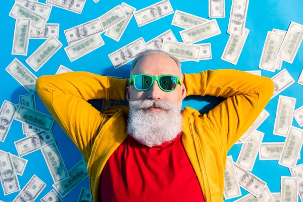 Yüksek açılı fotoğraf mutlu iyi ruh hali pozitif büyükbaba güneş gözlüğü içinde yerde yatıyor para mavi arka planda izole — Stok fotoğraf