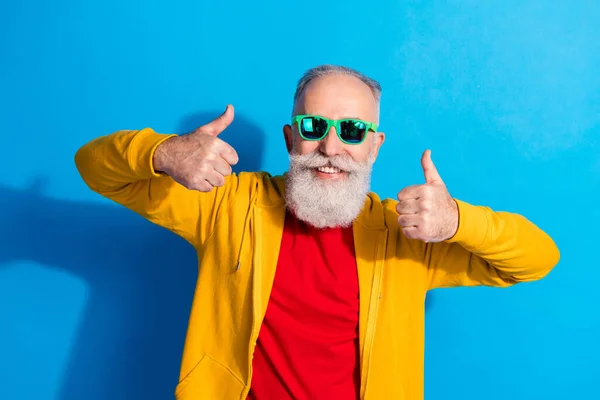 Foto de alegre sonriente abuelo de buen humor en gafas de sol que muestra el pulgar hacia arriba aislado sobre fondo de color azul —  Fotos de Stock