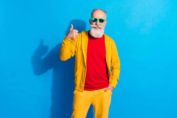 Foto de la persona positiva alegre sonrisa dentada mostrar el pulgar hacia arriba poner la mano en el bolsillo aislado en el fondo de color azul —  Fotos de Stock