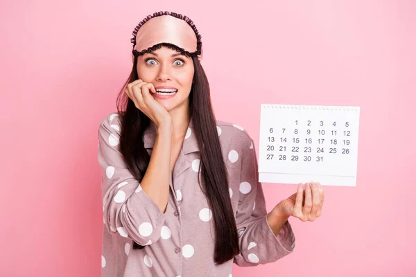 Photo of guilty scared young woman sleepwear biting fingers holding paper calendar isolated pink color background — Φωτογραφία Αρχείου