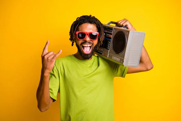 Foto de hombre joven emocionado disfrutar de música rock muestra cuerno rockero mantenga boombox aislado sobre fondo de color amarillo —  Fotos de Stock