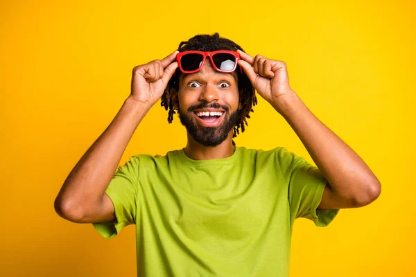 Фото молодого афрочеловека руки касаются солнцезащитных очков счастливый положительный удивленный продажа новости изолированы на желтом фоне цвета — стоковое фото