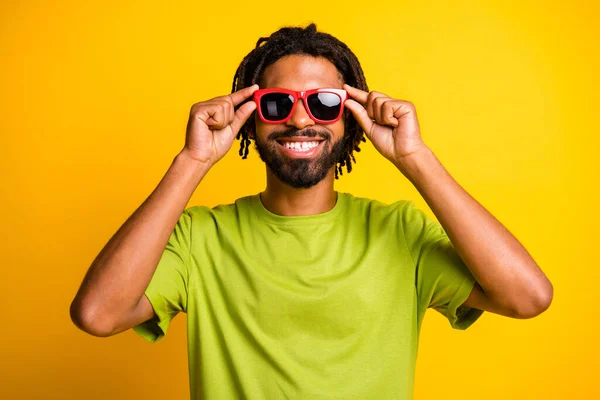 Foto de joven guapo hombre feliz sonrisa positiva manos toque gafas de sol viaje de verano aislado sobre fondo de color amarillo —  Fotos de Stock