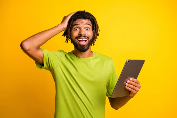 Foto de joven hombre guapo sorprendido agarre tableta mano tacto cabeza aislada sobre fondo de color amarillo —  Fotos de Stock