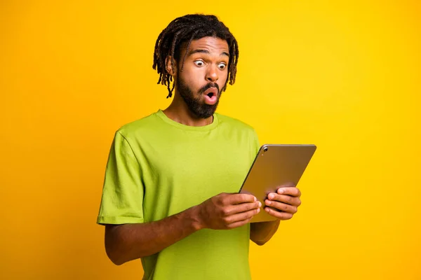 Foto de un joven africano sujetar la tableta sorprendido sorprendido información de noticias aisladas sobre fondo de color amarillo — Foto de Stock