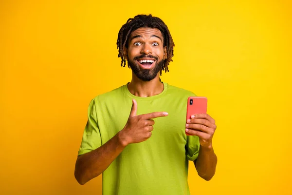 Foto van opgewonden donkere huid guy wijzen index vinger copyspace dragen groene t-shirt geïsoleerd over helder gele kleur achtergrond — Stockfoto