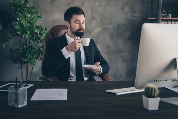 Foto van vreedzame bebaarde zakenman zit bureau hold cup geur thee aroma slijtage pak overhemd das in modern kantoor binnen — Stockfoto